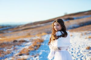Bride looks over her shoulder towards the camera.  She wears a white dress and a white faux fur stole in a winter wonderland.