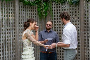 Bride, groom and the officiant stand at the alter. Bride is wiping away tears as groom says his vows.