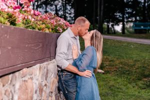 A romantic couple embraces against a stone wall with pink blossoms in the background.