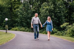 Couple walking hand in hand down a curved path surrounded by green trees.