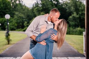 A couple in denim and gray share a romantic dip pose on an outdoor pathway.