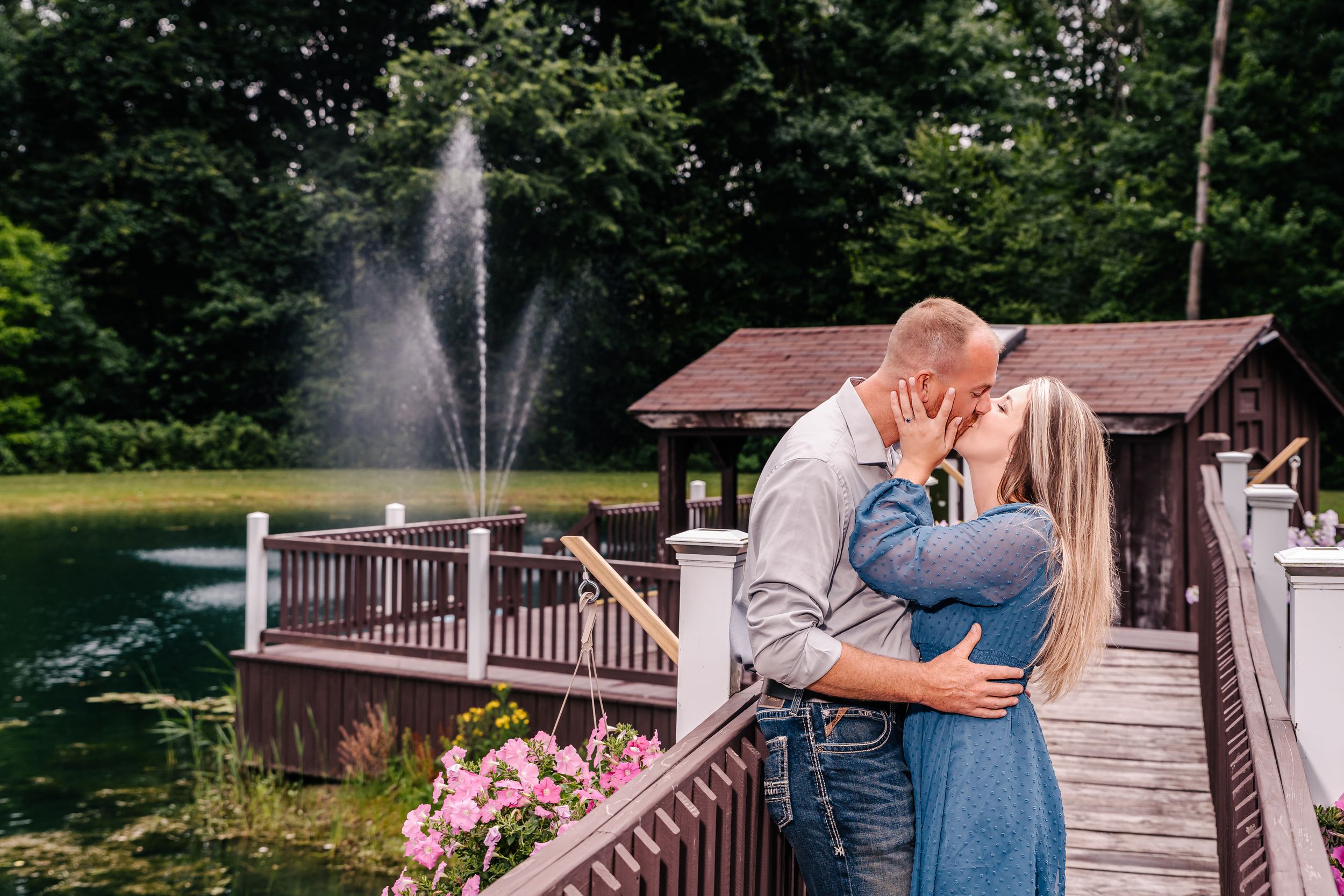 A romantic moment captured on a wooden bridge with a water fountain and pond backdrop.