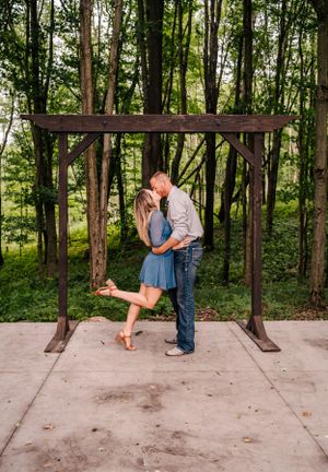 A couple shares a romantic kiss under a wooden archway in a forest setting.