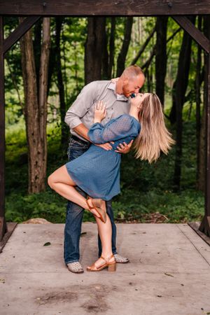 A couple performs a romantic dip pose under a wooden archway.