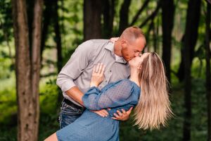 A couple shares a passionate dip kiss against a forest backdrop.