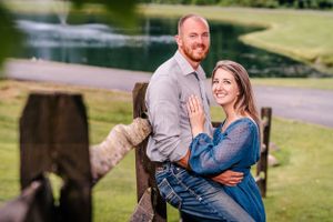 A couple shares a joyful moment by a wooden fence with one showing off an engagement ring.