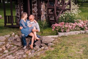 A couple sits on stone steps near a rustic cabin with pink flowers blooming nearby.