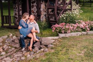 Two people share an intimate moment while sitting on stone steps by a rustic cabin with flowers.