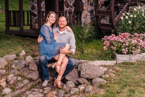 A couple relaxes on stone steps near a rustic cabin surrounded by pink flowers.