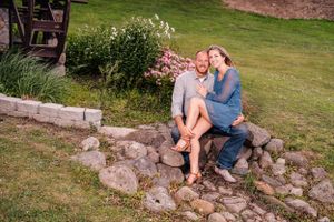 A couple shares a laugh while sitting on decorative stone steps near flowering plants.