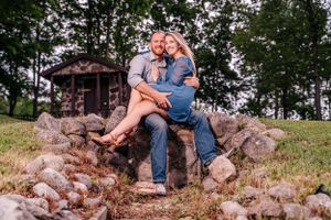 A couple sits together on stone steps with a rustic cabin in the background.