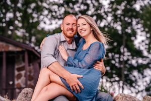 A casual couple sits on rocks together during an outdoor portrait session at sunset.