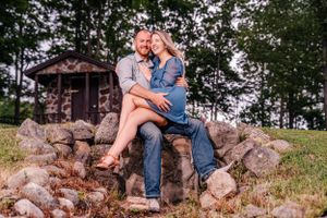 A couple embraces on stone steps with a rustic cabin and trees in the background.