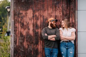 A couple stands against a rustic red barn door sharing a tender moment.