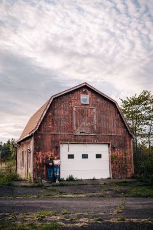 A rustic red barn with white garage door stands beneath a cloudy sky.