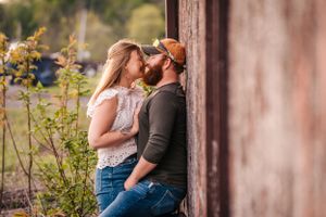 A romantic couple shares an intimate moment against a wooden wall in golden light.
