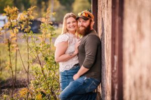 A couple poses together against a rustic backdrop with golden plants nearby.