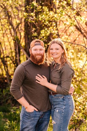 A couple in casual attire poses together against a golden autumn forest backdrop.