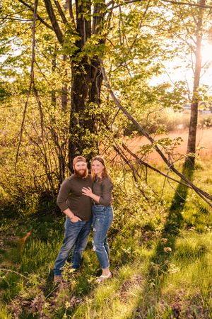 A romantic outdoor portrait with sunlit trees and tall grass in the background.