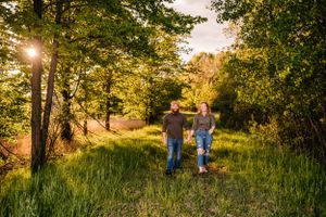 Two people stroll together on a grassy trail surrounded by trees at sunset.