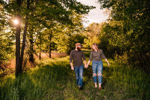 A couple walks hand in hand through a sun-dappled woodland path.