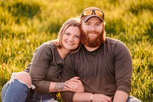 A couple sits together in golden grass during sunset for a casual outdoor portrait.