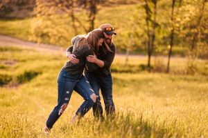 Two people share a playful moment in tall grass during golden hour.