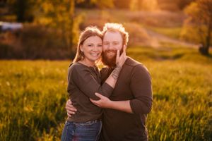 A couple embraces in casual clothing against a backdrop of golden sunset light.