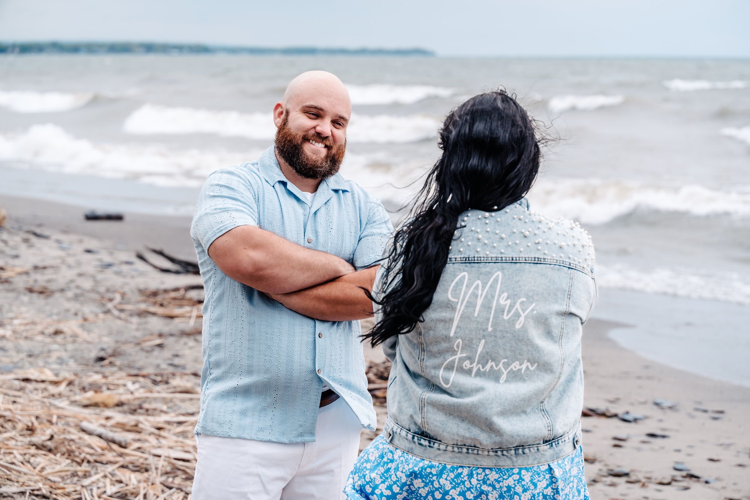 Two people standing on a beach by the ocean with one wearing a light gray jacket on a cloudy day.