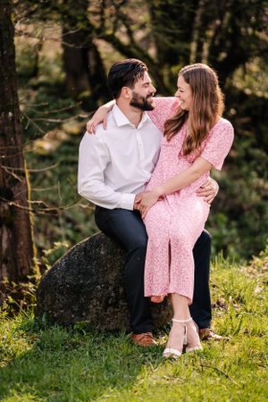 Couple sits on a rock in nature wearing coordinated pink and white outfits.