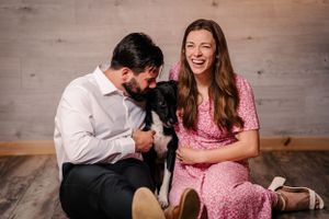 Candid moment with couple laughing while holding their black dog.