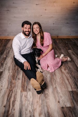 Casual portrait of couple with black dog sitting on hardwood floor.