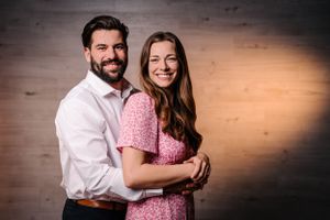 Romantic couple pose against wooden wall with dramatic lighting.
