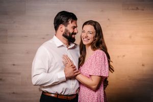 Couple sharing joyful moment against wooden wall in pink and white outfits.