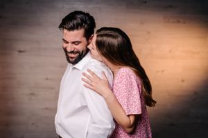 A couple in pink and white embraces in front of a rustic wooden backdrop at a photo shoot.