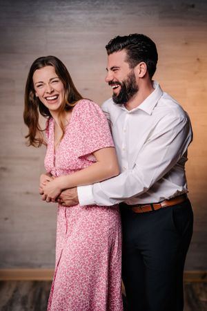 A joyful couple laughs together while embracing, wearing pink dress and white shirt.