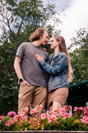 A couple shares an intimate moment in front of pink flowers and trees on a summer day.
