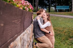 A tender embrace captured near a stone wall adorned with pink flowers in an outdoor garden.