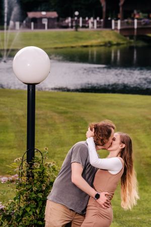 A romantic moment captured by a white globe lamppost near a fountain in a park.