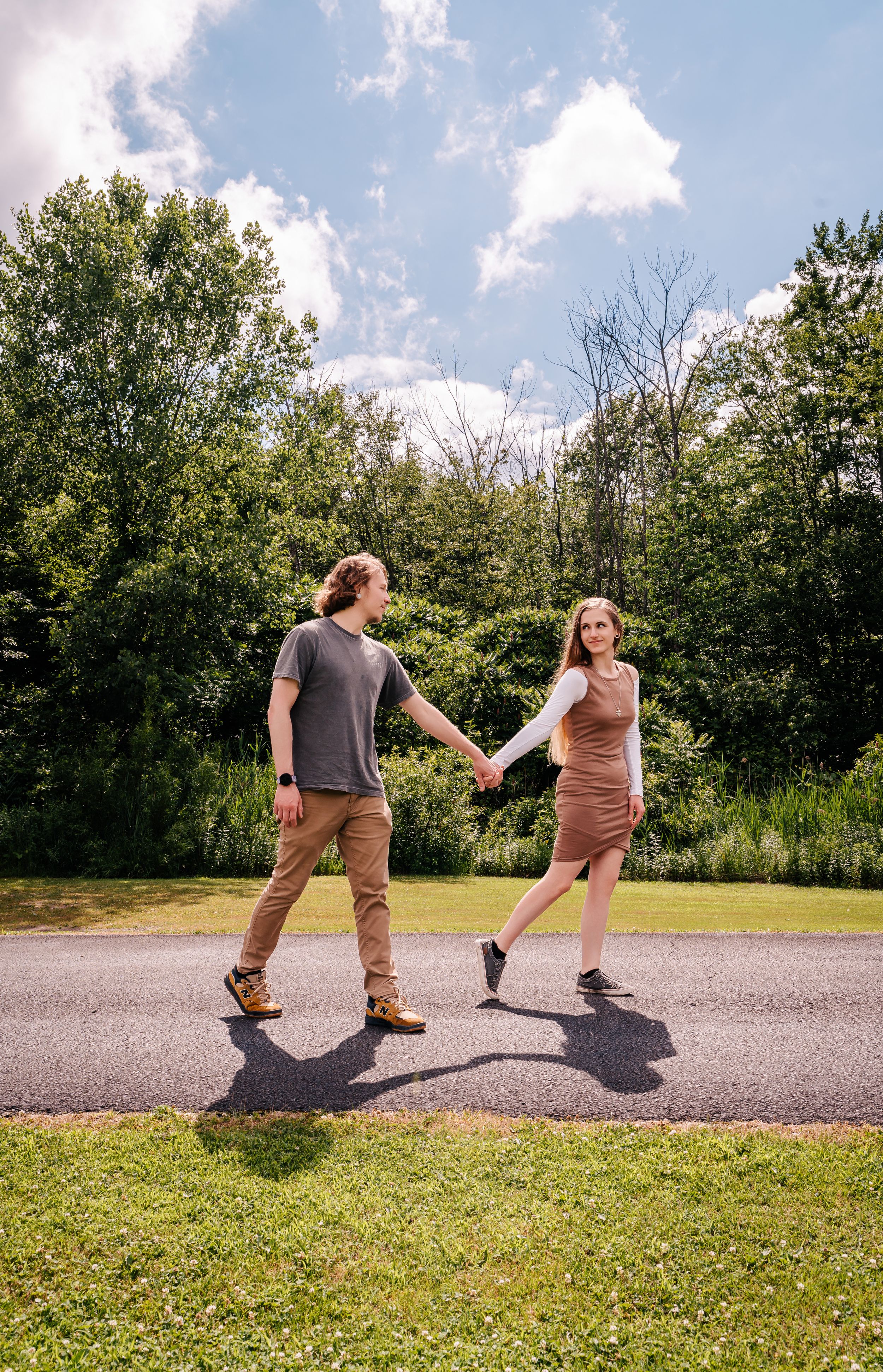 A couple holds hands while walking on a path surrounded by lush greenery.