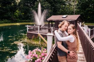 A couple shares a romantic moment on a wooden deck over a pond with a fountain.
