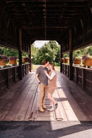 A couple embraces in a rustic covered bridge with sunlight streaming through.