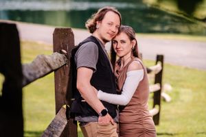 An affectionate couple embracing against a wooden fence in nature.