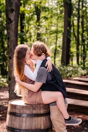 A romantic moment shared while sitting on a rustic wooden barrel in the woods.