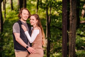 A couple in casual attire posing together against a wooded backdrop.