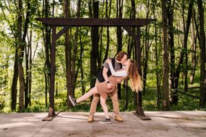 A playful dance dip pose under a wooden archway in the forest.