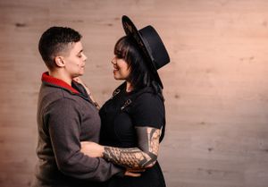 A couple in contrasting outfits share an intimate moment against a wooden wall backdrop.