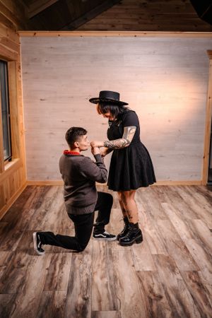 A proposal scene on wooden floors with one person kneeling before another in a black dress.