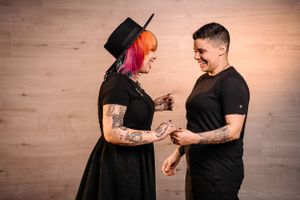 Alternative couple in black clothing sharing a playful moment against wooden wall background.