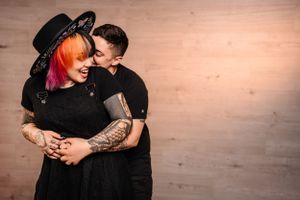 Intimate portrait of couple in black clothing embracing against wooden wall.